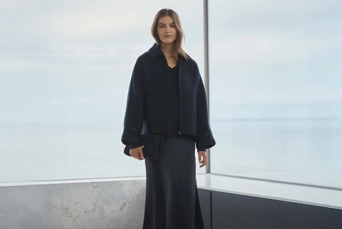 Woman in navy wool jacket holding a clutch by floor-to-ceiling windows