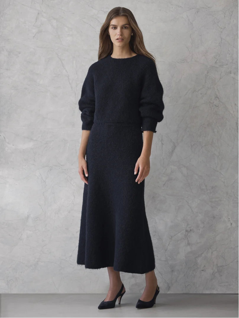 Woman in navy knit jumper and midi skirt against a marble backdrop